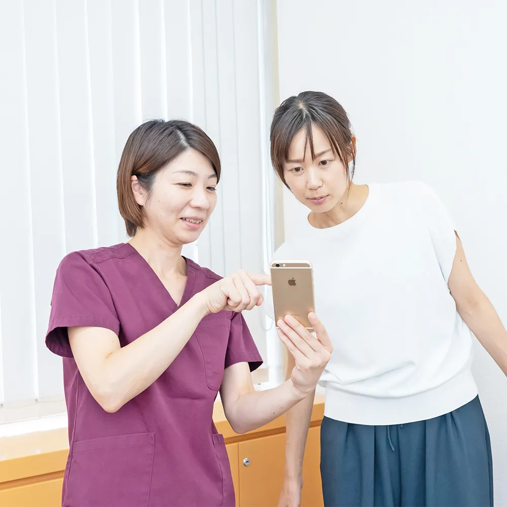 女性にスマホの画像を見せて説明する整体師